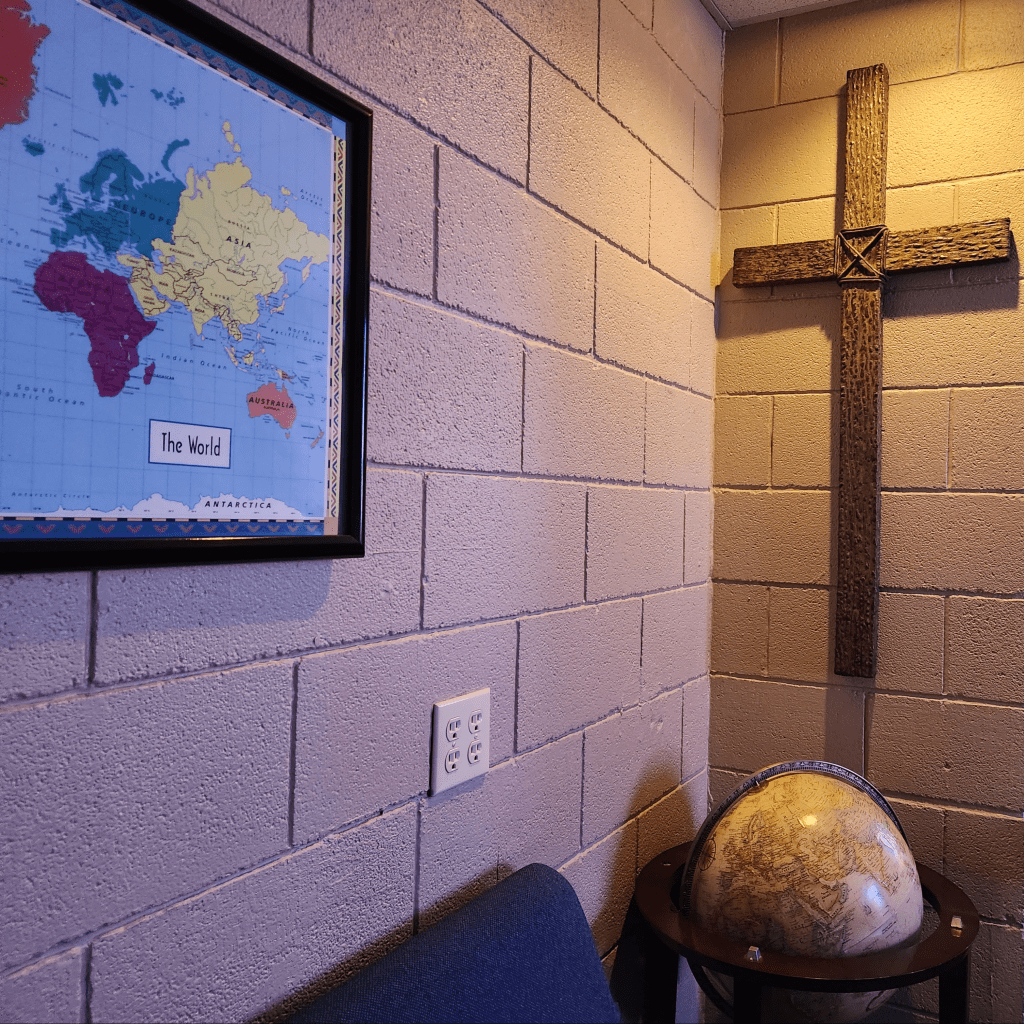 A cross on a wall, facing a map of the world.  A globe sits beneath the cross.